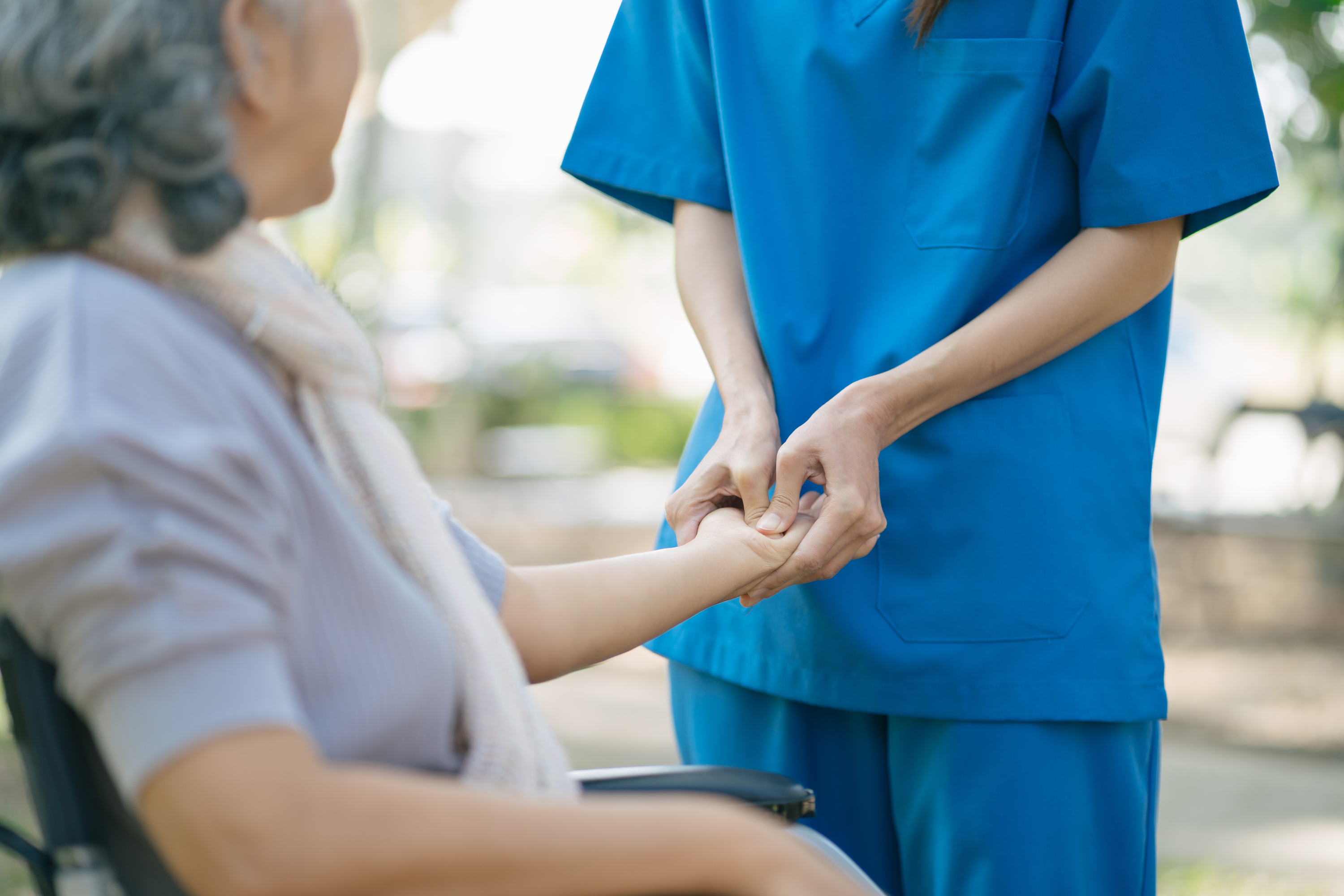 Pflegerin hält Hand von Seniorin
